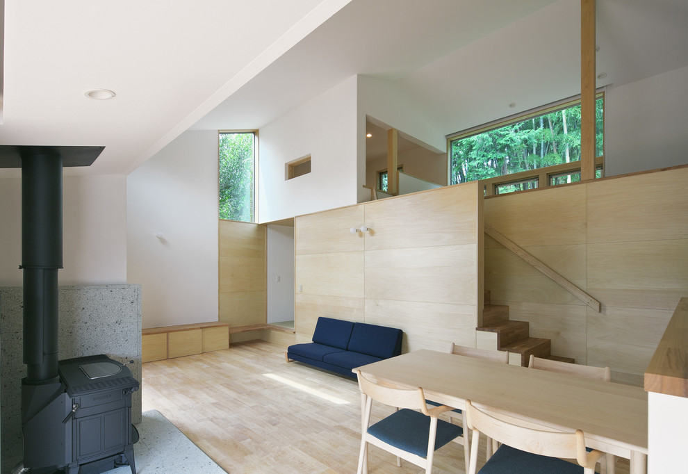 Idee per una sala da pranzo aperta verso il soggiorno scandinava con pareti bianche, parquet chiaro, stufa a legna e cornice del camino in pietra