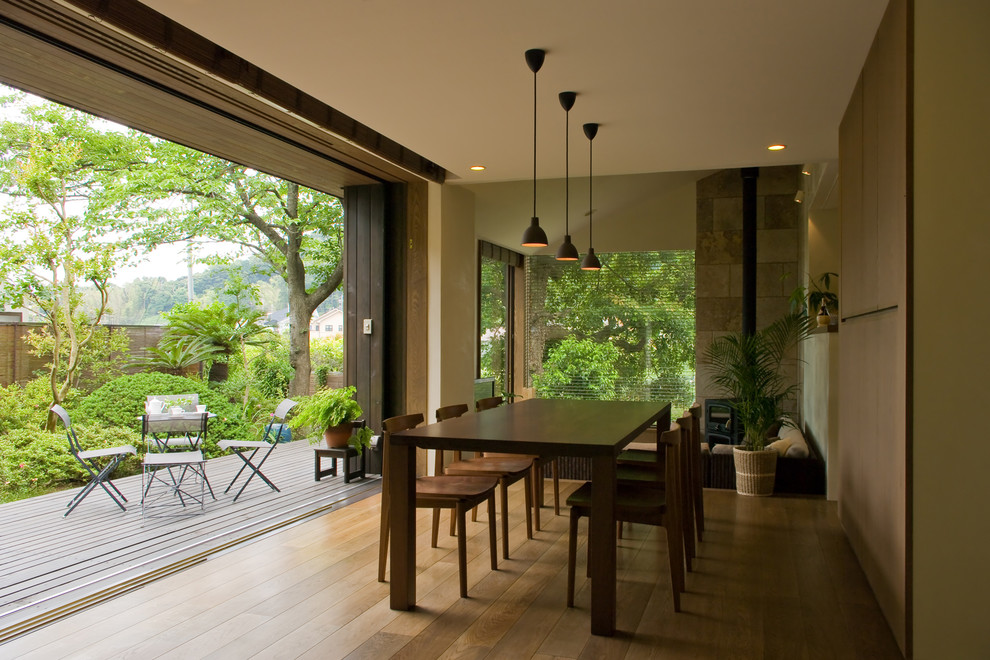 Idée de décoration pour une salle à manger ouverte sur le salon asiatique de taille moyenne avec un mur blanc, un sol en bois brun, un poêle à bois, un manteau de cheminée en pierre et un sol marron.