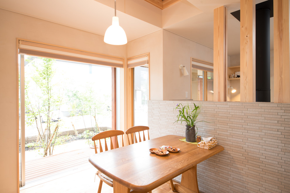 Foto di una sala da pranzo aperta verso la cucina etnica con pareti beige, pavimento in legno massello medio, stufa a legna e cornice del camino piastrellata