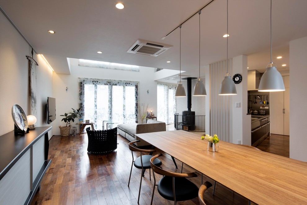 Foto di una sala da pranzo aperta verso il soggiorno design con pareti bianche, pavimento in legno massello medio, stufa a legna e pavimento marrone
