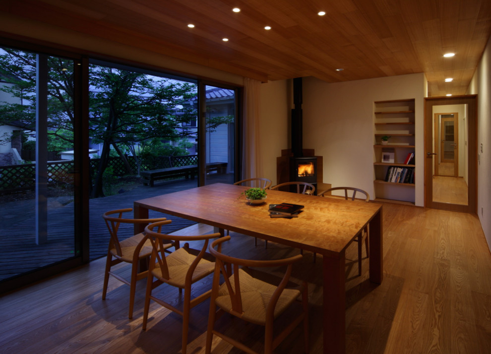 Inspiration pour une salle à manger minimaliste fermée et de taille moyenne avec un mur blanc, un sol en bois brun, un poêle à bois, un manteau de cheminée en carrelage et un sol marron.