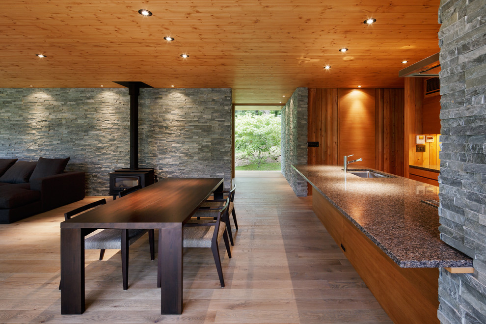 Foto de comedor minimalista abierto con paredes grises, suelo de madera en tonos medios, estufa de leña y marco de chimenea de piedra