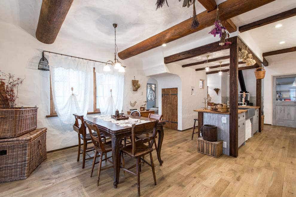 Immagine di una sala da pranzo aperta verso il soggiorno mediterranea di medie dimensioni con pareti bianche, parquet chiaro, stufa a legna, cornice del camino in mattoni e pavimento marrone