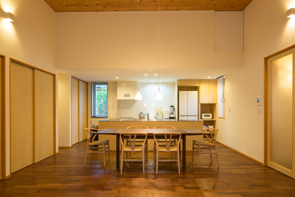 Cette image montre une salle à manger ouverte sur le salon asiatique de taille moyenne avec un mur blanc, parquet foncé, un poêle à bois, un manteau de cheminée en plâtre et un sol marron.