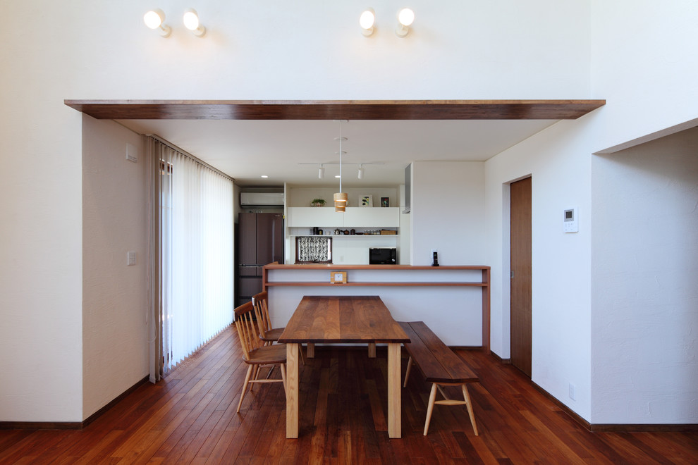 Cette photo montre une salle à manger ouverte sur le salon tendance avec un mur blanc, parquet foncé et un sol marron.