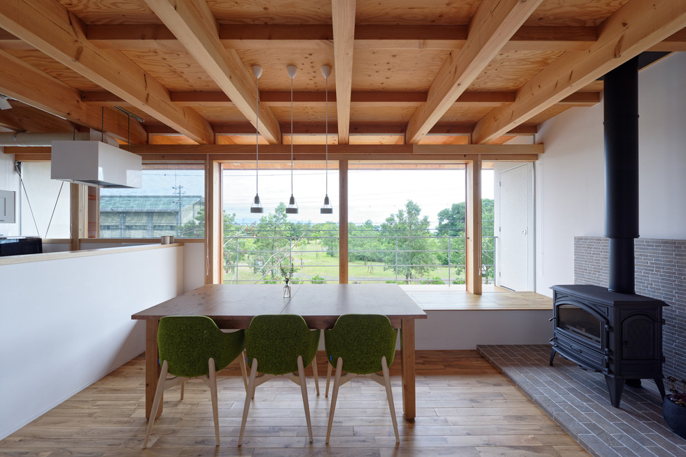 Modelo de comedor de cocina de estilo zen con paredes blancas, suelo de madera en tonos medios, estufa de leña, marco de chimenea de baldosas y/o azulejos y suelo marrón