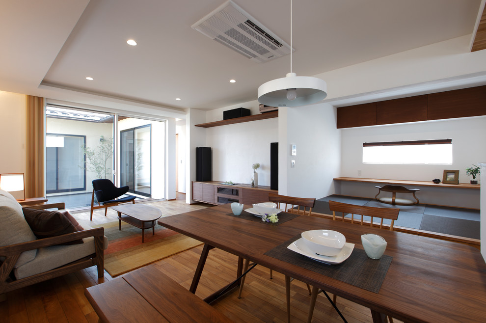 Diseño de comedor asiático abierto con paredes blancas, suelo de madera en tonos medios y suelo marrón