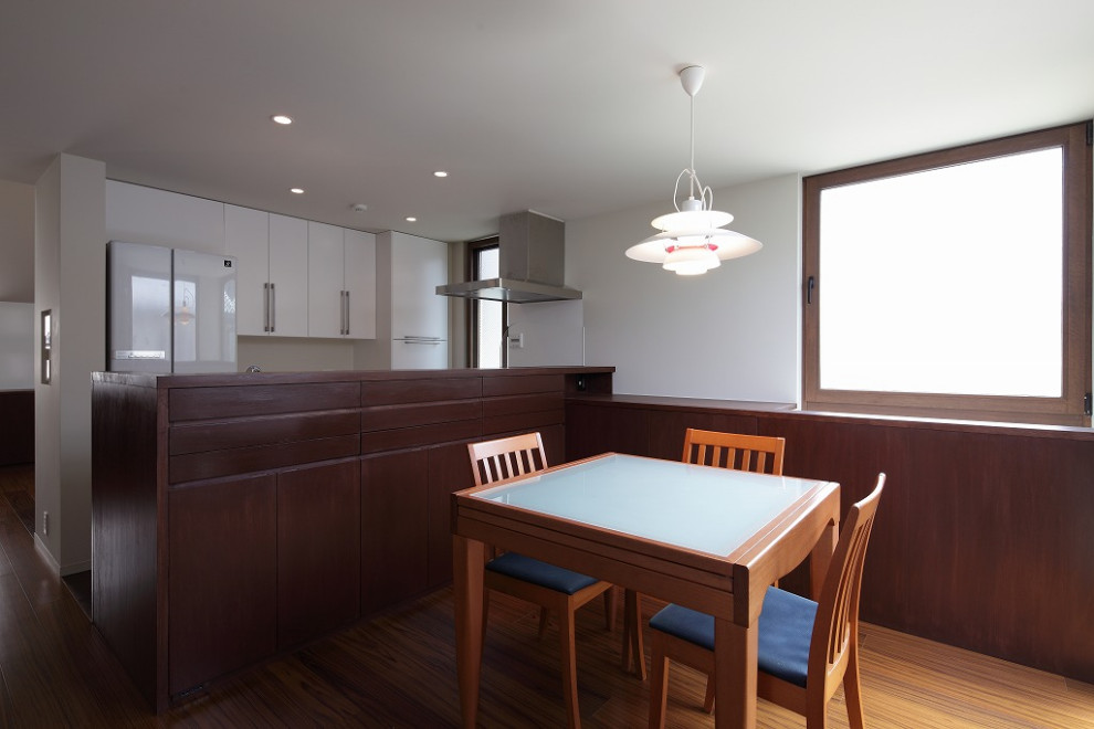 Aménagement d'une petite salle à manger ouverte sur la cuisine avec un mur blanc, un sol en contreplaqué, une cheminée double-face et un sol marron.