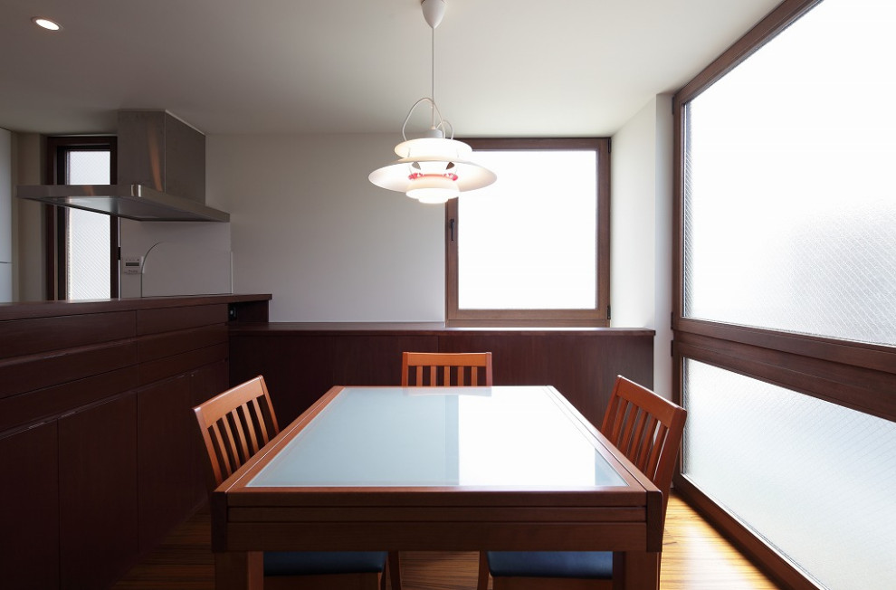 Cette image montre une petite salle à manger ouverte sur la cuisine avec un mur blanc, un sol en contreplaqué, une cheminée double-face et un sol marron.