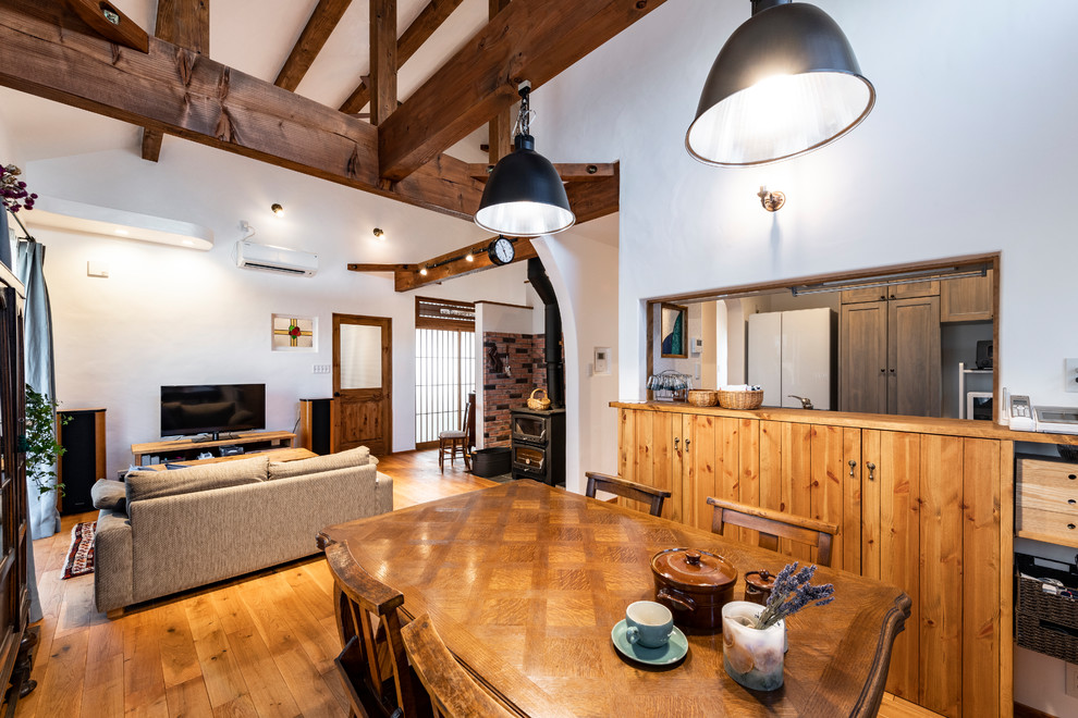 Aménagement d'une salle à manger ouverte sur le salon campagne de taille moyenne avec un mur blanc, parquet clair, un poêle à bois, un manteau de cheminée en brique et un sol marron.