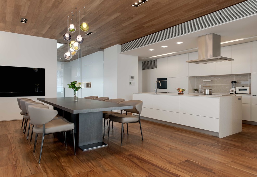 Cette image montre une salle à manger ouverte sur la cuisine design de taille moyenne avec un mur blanc, un sol en bois brun et aucune cheminée.