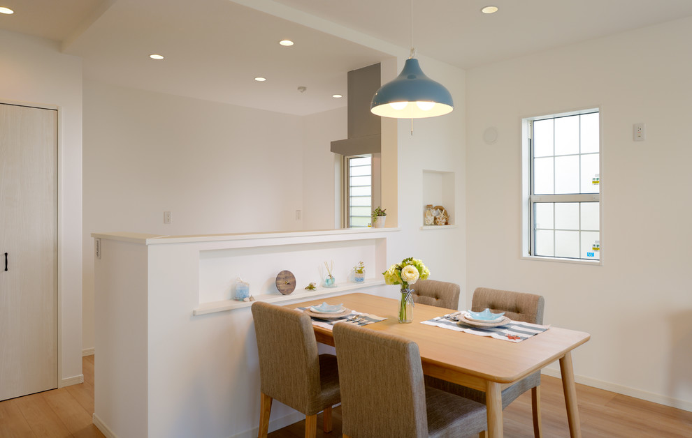 Cette image montre une salle à manger ouverte sur la cuisine avec un mur blanc, un sol en contreplaqué et un sol beige.
