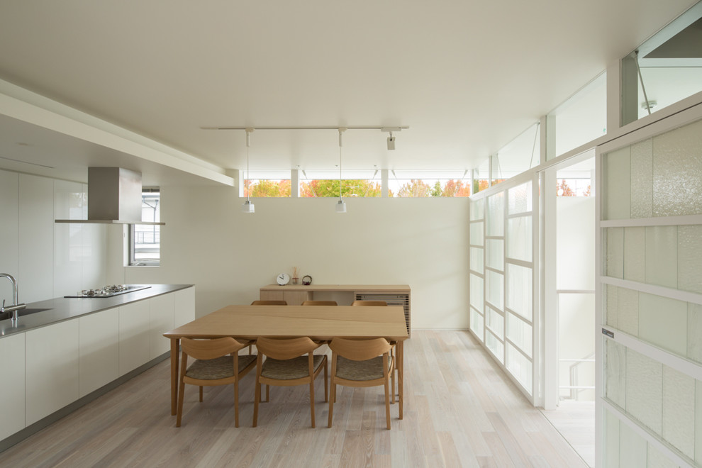 Modern inredning av en matplats med öppen planlösning, med vita väggar, ljust trägolv och vitt golv