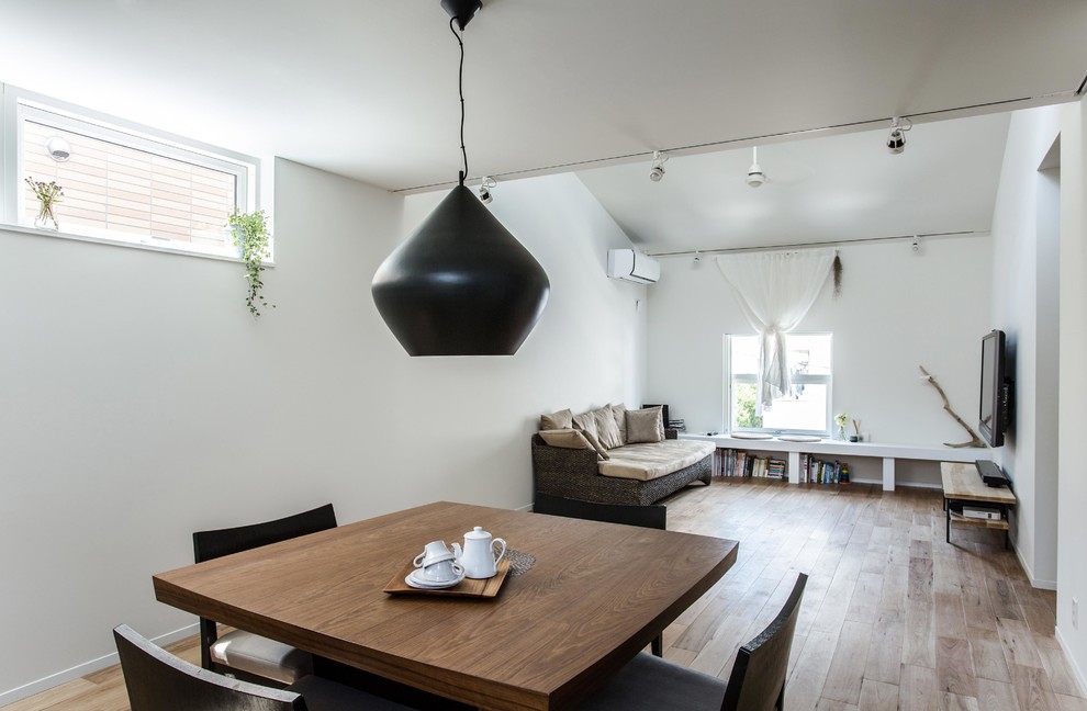 Cette image montre une salle à manger ouverte sur le salon nordique avec un mur blanc, un sol en bois brun et un sol marron.