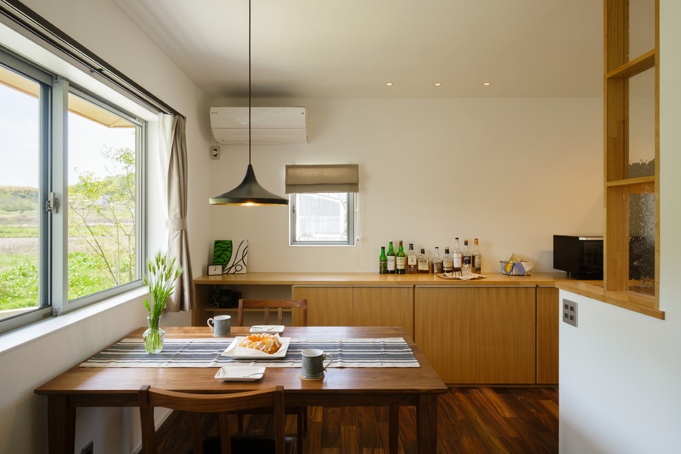 Cette photo montre une petite salle à manger tendance avec un mur blanc, parquet foncé et un sol marron.