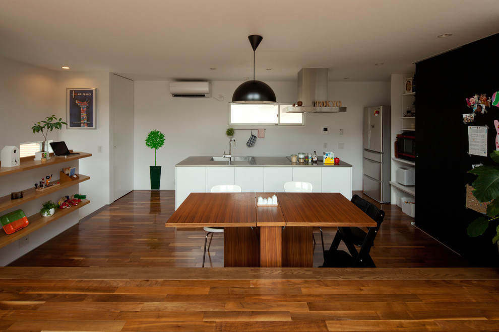Cette image montre une salle à manger ouverte sur le salon minimaliste de taille moyenne avec un mur blanc, parquet foncé et un sol marron.