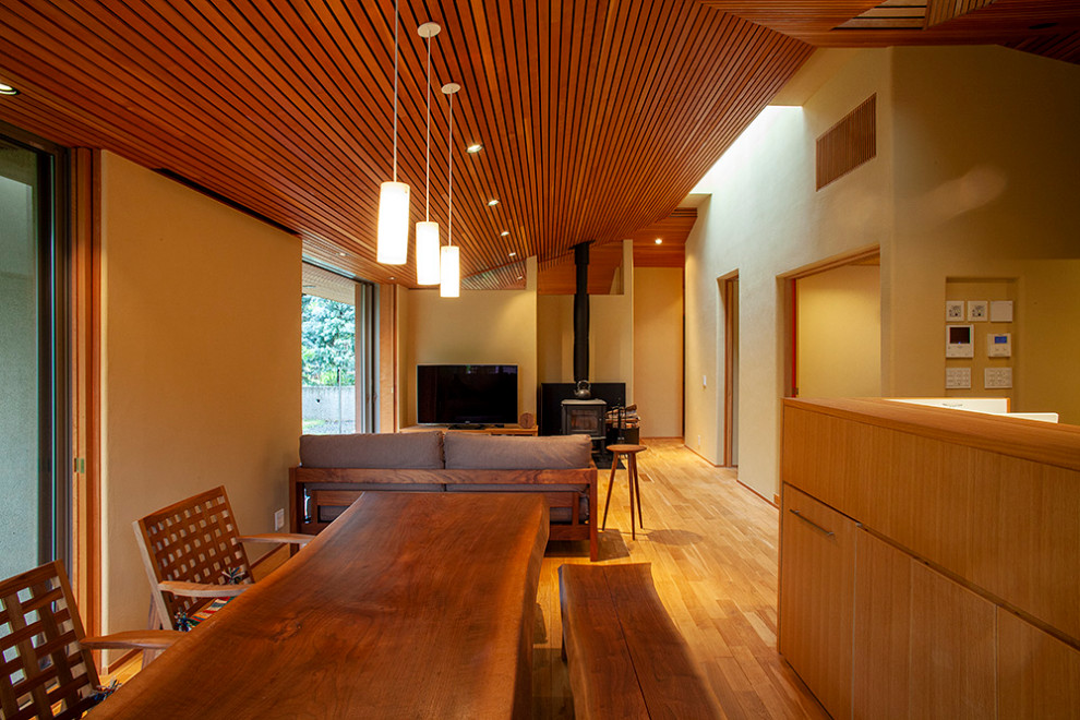 Esempio di una sala da pranzo aperta verso il soggiorno minimalista di medie dimensioni con pareti beige, parquet scuro, stufa a legna, pavimento marrone e cornice del camino in pietra
