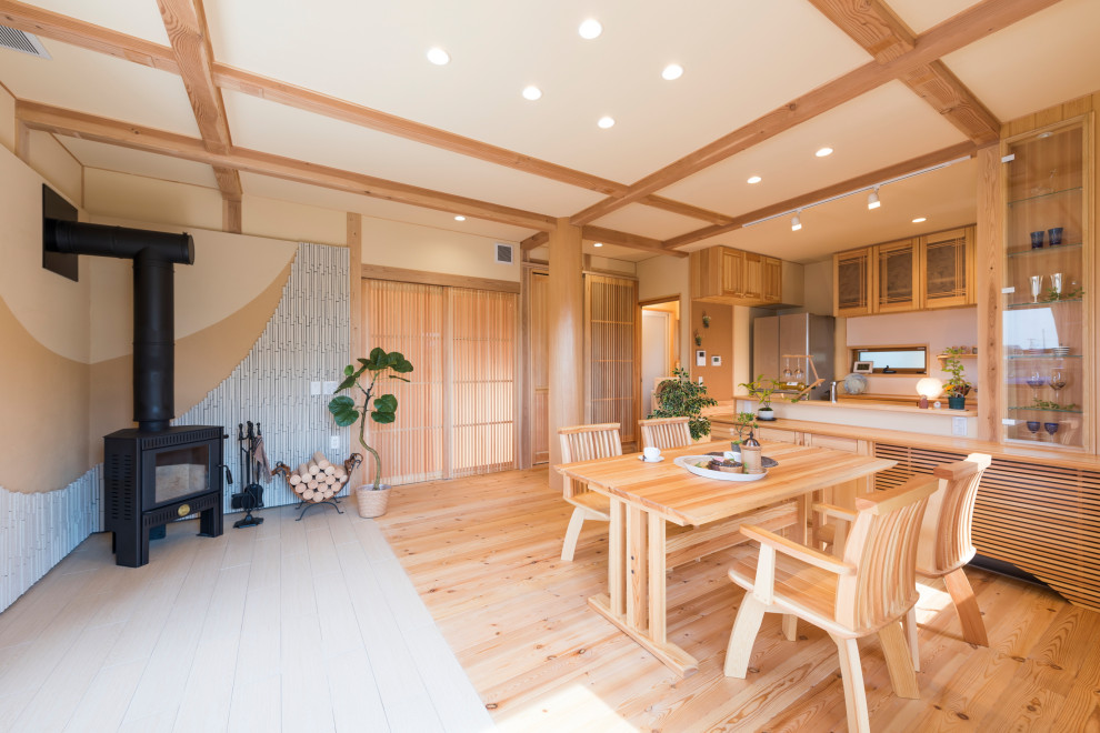 Aménagement d'une salle à manger asiatique avec un mur beige, parquet clair, un poêle à bois, un sol beige et poutres apparentes.