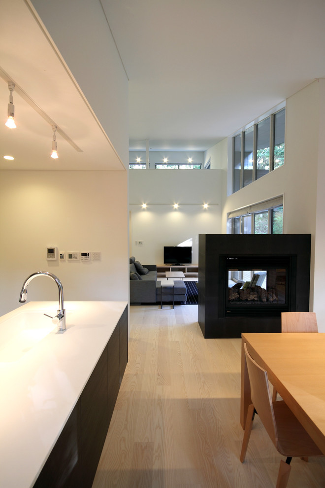 Immagine di una sala da pranzo aperta verso la cucina moderna di medie dimensioni con pareti bianche, pavimento in compensato, camino bifacciale, cornice del camino in pietra e pavimento marrone