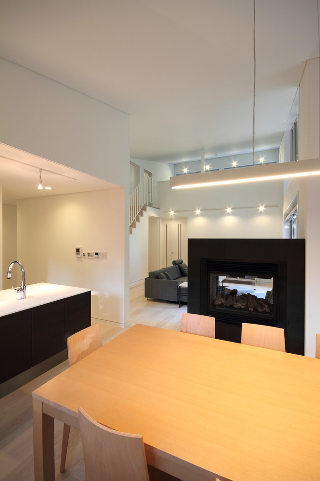 Источник вдохновения для домашнего уюта: кухня-столовая среднего размера в стиле модернизм с белыми стенами, полом из фанеры, двусторонним камином, фасадом камина из камня и коричневым полом