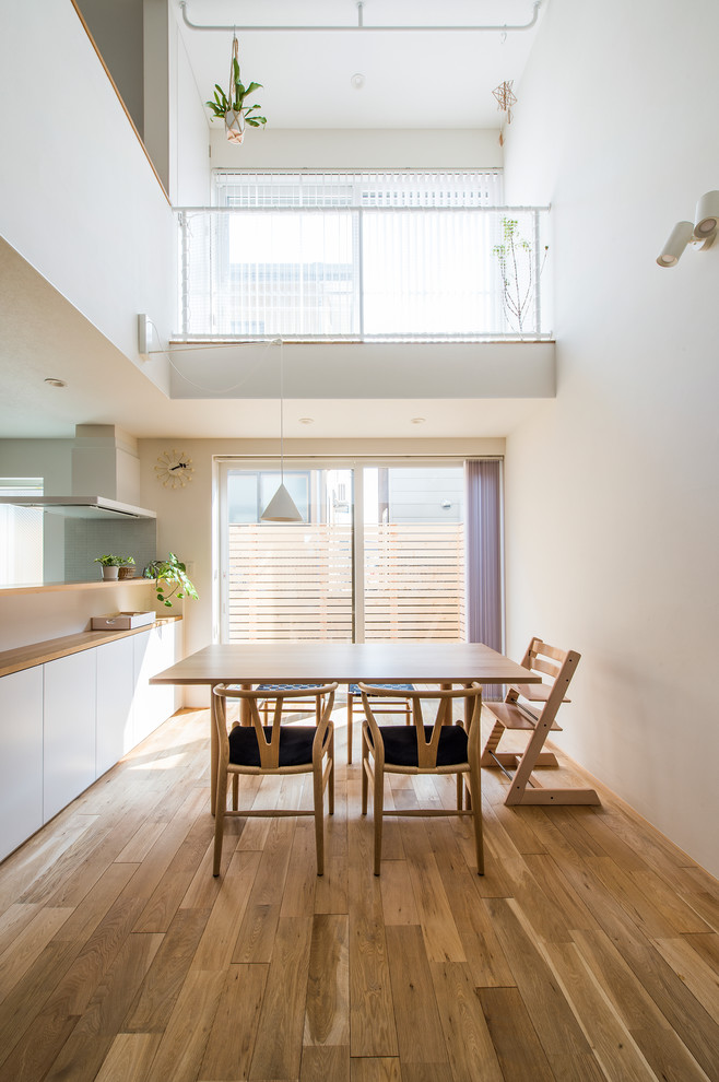 Cette photo montre une salle à manger ouverte sur le salon scandinave avec un mur blanc, un sol en bois brun et un sol marron.