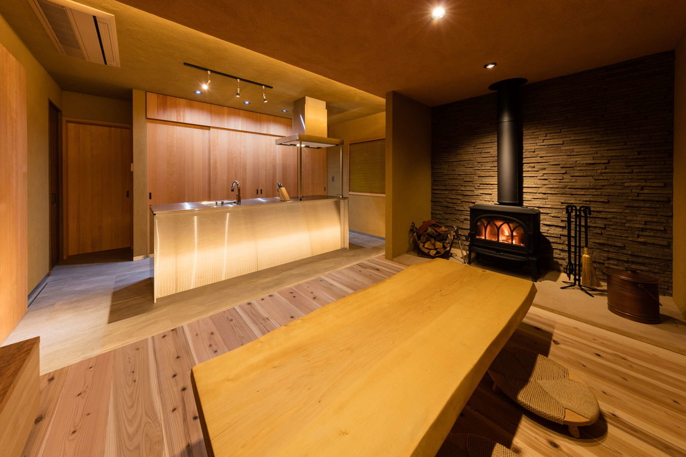 Exemple d'une salle à manger ouverte sur la cuisine asiatique avec un sol en bois brun, un poêle à bois et un manteau de cheminée en pierre.