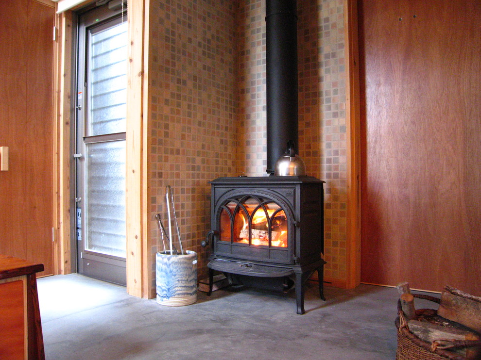他の地域にある中くらいな和風のおしゃれなLDK (茶色い壁、コンクリートの床、薪ストーブ、タイルの暖炉まわり、グレーの床) の写真