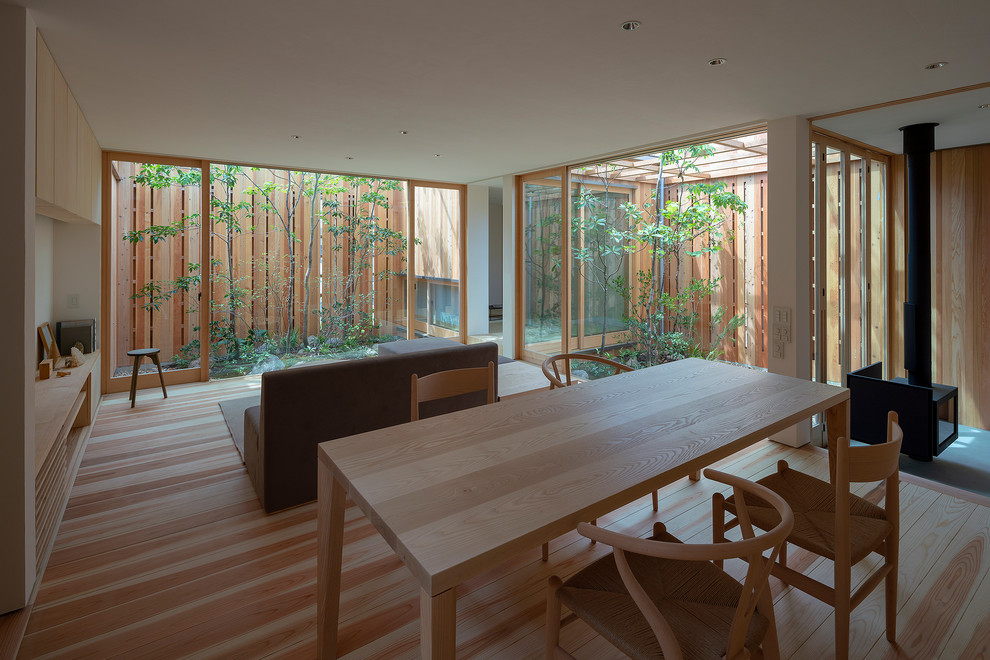 Cette photo montre une salle à manger ouverte sur le salon asiatique de taille moyenne avec un mur blanc, parquet peint, un poêle à bois, un manteau de cheminée en béton et un sol marron.