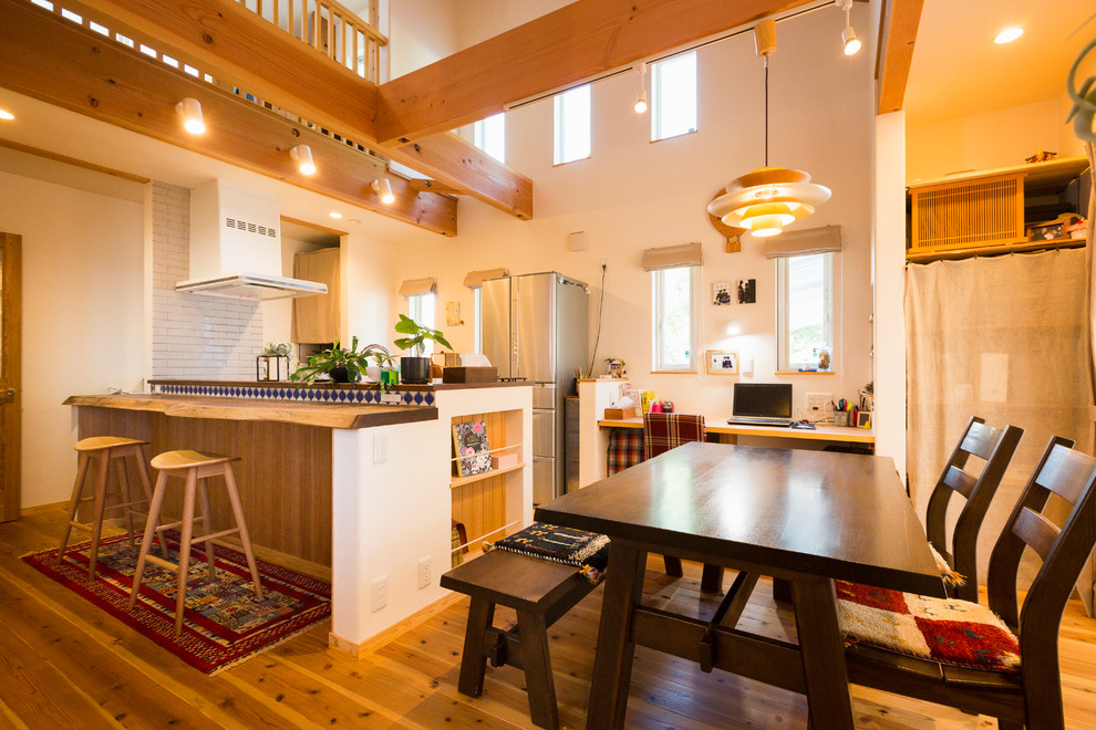 Cette photo montre une salle à manger ouverte sur la cuisine asiatique avec un mur blanc, un sol en bois brun, un poêle à bois, un manteau de cheminée en brique et un sol marron.