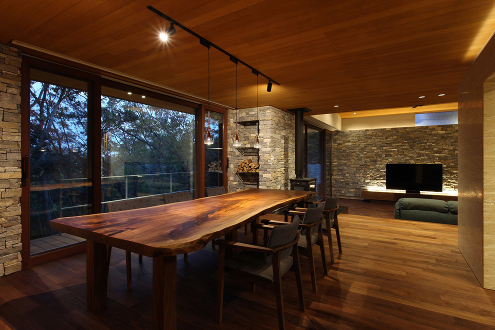 Exemple d'une salle à manger ouverte sur le salon moderne avec un mur gris, un sol en bois brun, un sol marron, un manteau de cheminée en pierre et un plafond en bois.