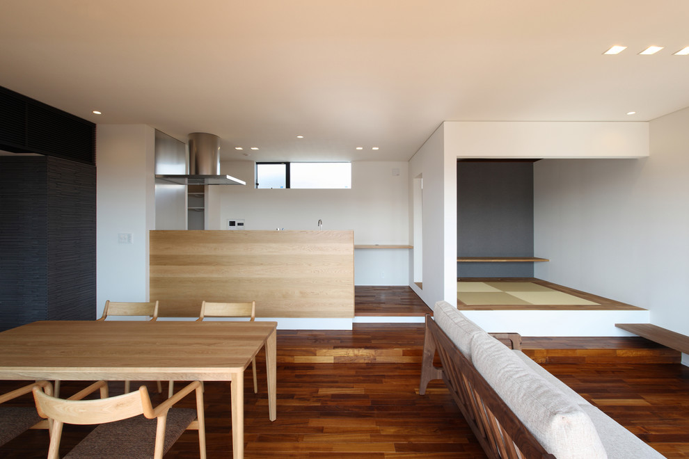 Modelo de comedor minimalista abierto con paredes blancas, suelo de madera oscura y suelo marrón