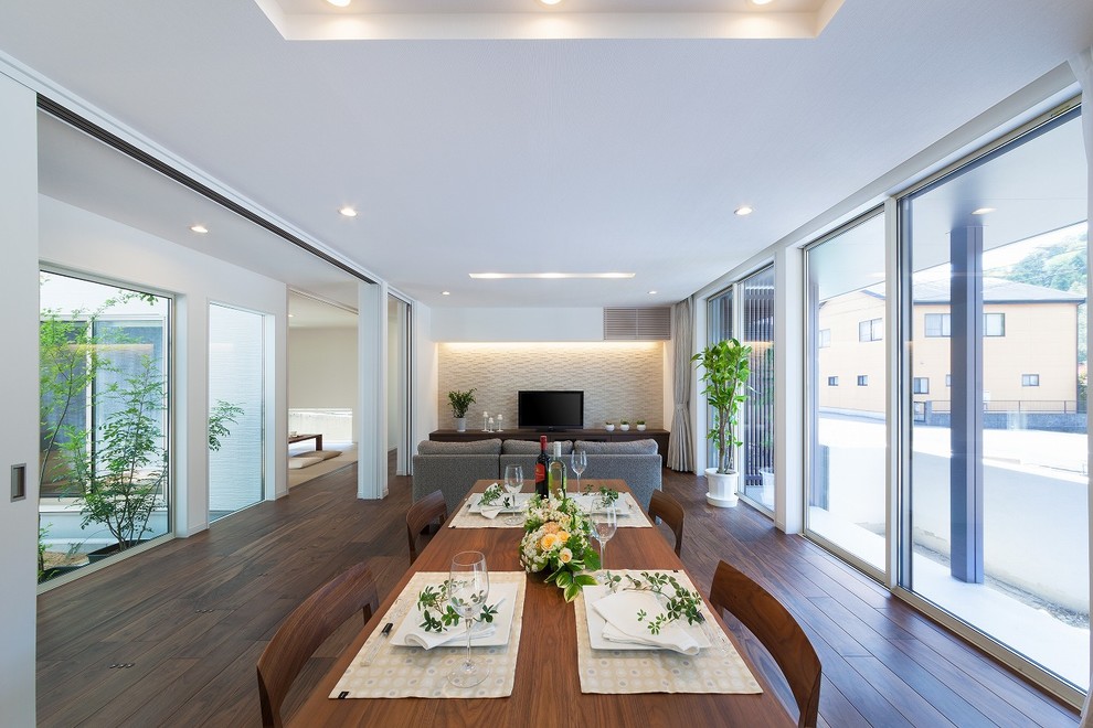 Ispirazione per una sala da pranzo aperta verso il soggiorno minimalista con pareti bianche, parquet scuro e pavimento marrone