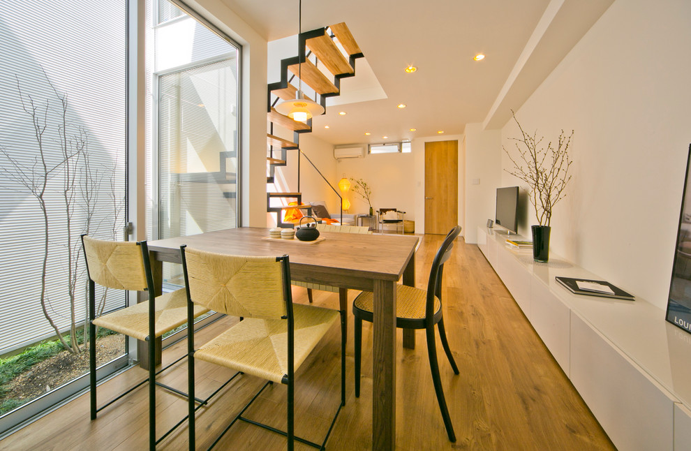 Foto di una sala da pranzo aperta verso il soggiorno minimalista con pareti bianche, pavimento in legno massello medio e pavimento marrone