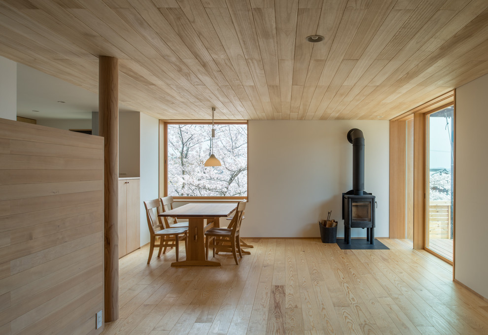Foto de comedor nórdico abierto con paredes blancas, suelo de madera clara, estufa de leña y marco de chimenea de metal