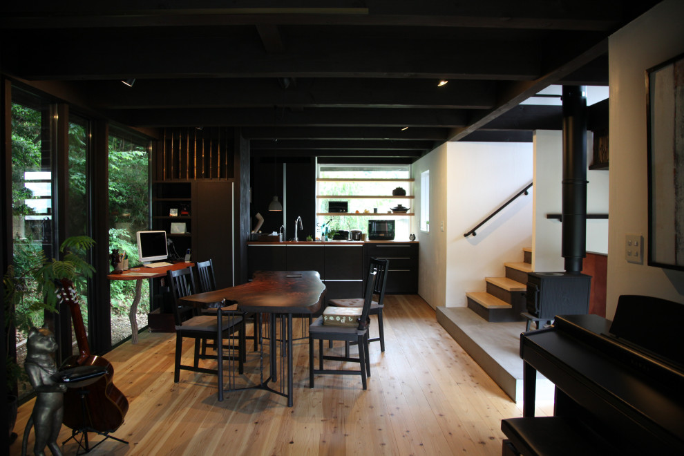 Cette image montre une salle à manger ouverte sur le salon asiatique de taille moyenne avec un mur blanc, un sol en bois brun, un poêle à bois, un manteau de cheminée en plâtre et poutres apparentes.