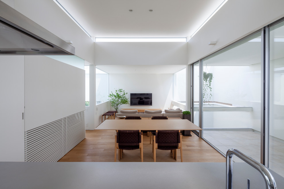 Diseño de comedor contemporáneo abierto con paredes blancas, suelo de madera en tonos medios y suelo marrón