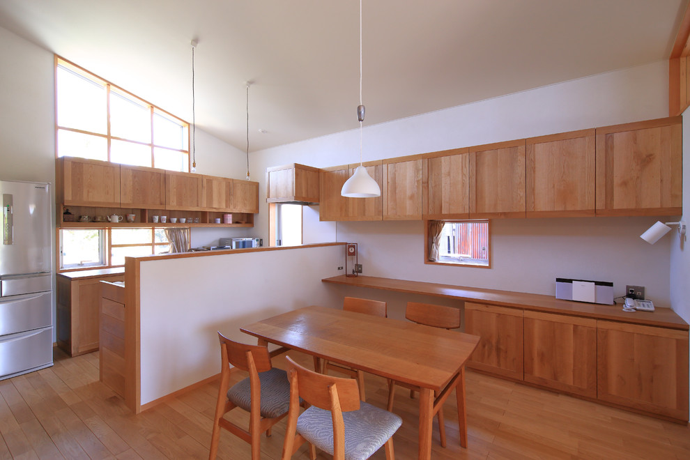 Réalisation d'une salle à manger ouverte sur la cuisine minimaliste avec un mur blanc, un sol en bois brun et un sol beige.