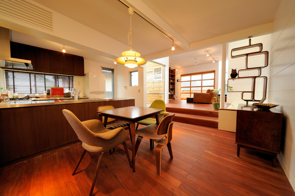 Foto di una sala da pranzo aperta verso il soggiorno minimalista con pareti bianche, pavimento in legno verniciato e pavimento marrone