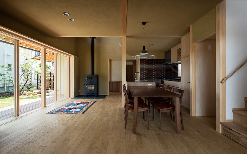 Modelo de comedor asiático abierto con paredes beige, suelo de madera clara, estufa de leña, marco de chimenea de baldosas y/o azulejos y suelo beige