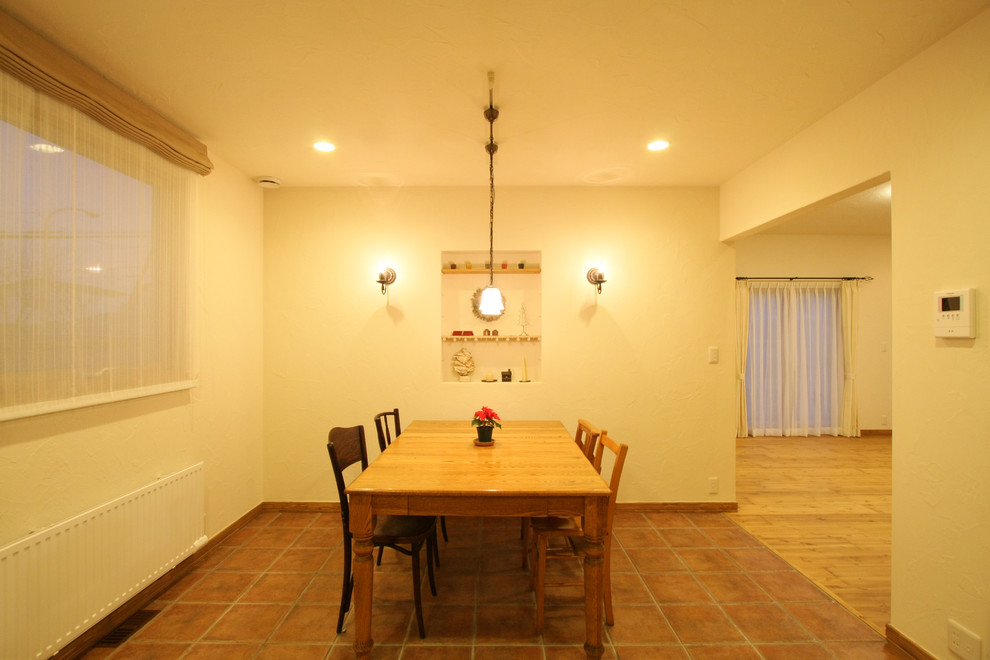 Exemple d'une salle à manger méditerranéenne avec un mur blanc, tomettes au sol et un sol marron.