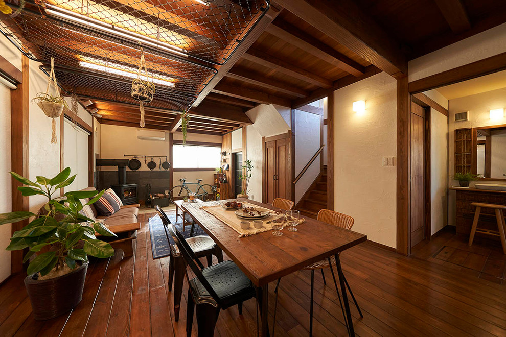 Réalisation d'une salle à manger ouverte sur le salon asiatique avec un poêle à bois, un manteau de cheminée en carrelage, un mur blanc, un sol en bois brun et un sol marron.