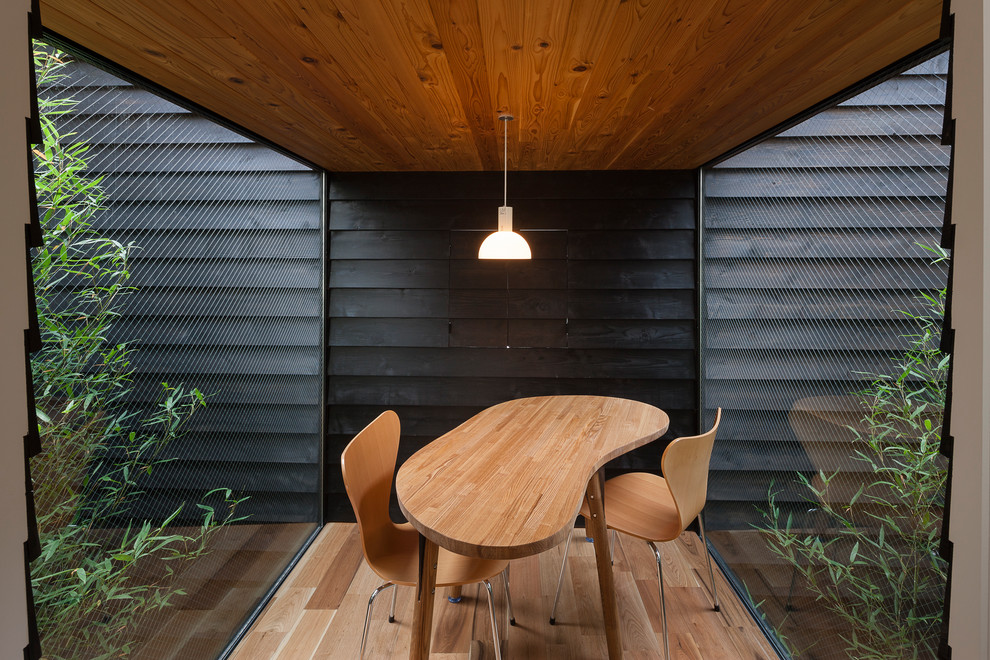 This is an example of a small world-inspired dining room in Tokyo with black walls, light hardwood flooring and brown floors.