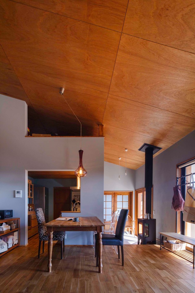 Imagen de comedor rural de tamaño medio abierto con paredes grises, suelo de madera en tonos medios, estufa de leña y suelo marrón