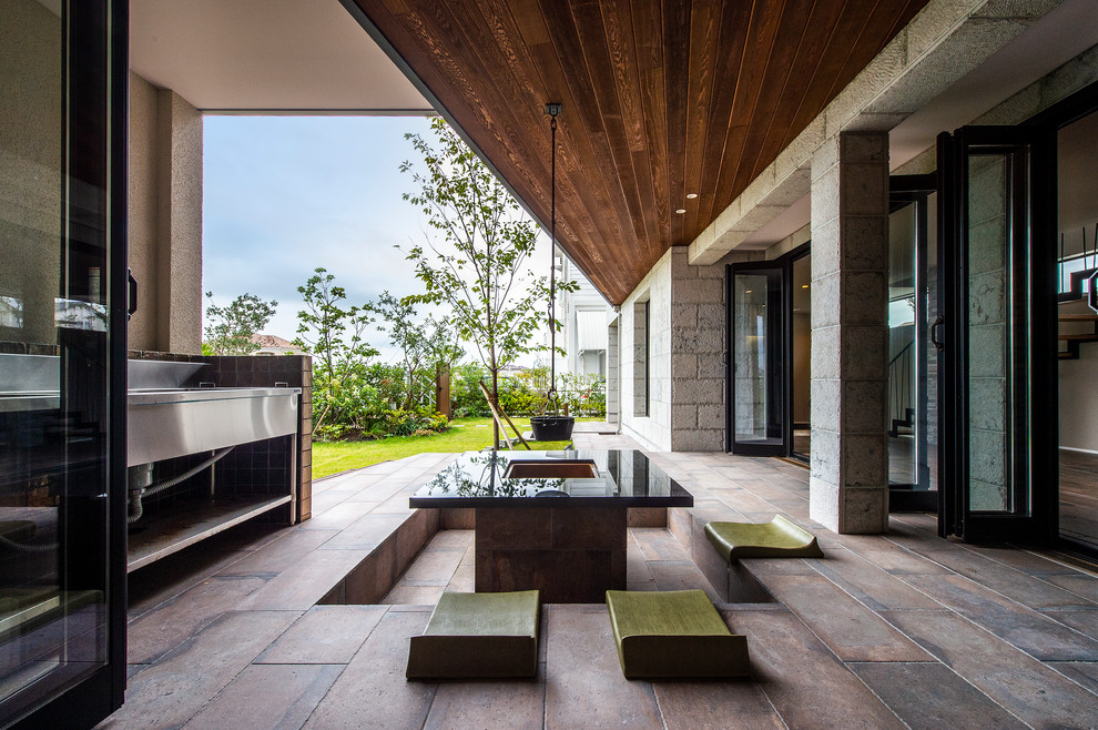 Immagine di un patio o portico minimalista di medie dimensioni e davanti casa con un focolare, piastrelle e un tetto a sbalzo