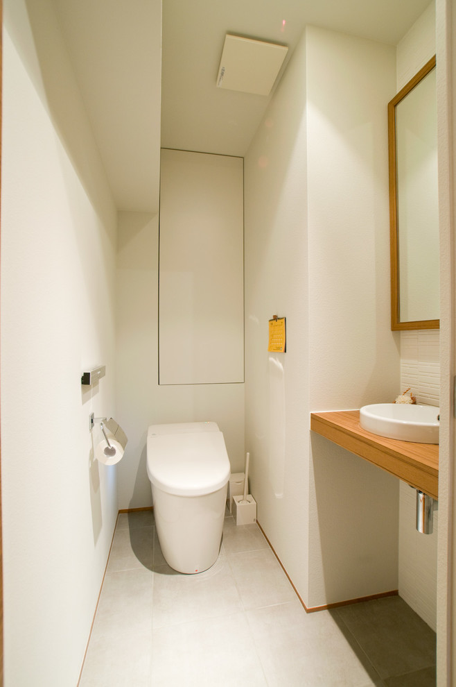 福岡にある小さな北欧スタイルのおしゃれなトイレ・洗面所 (白いタイル、白い壁、オーバーカウンターシンク、木製洗面台、グレーの床、ブラウンの洗面カウンター) の写真