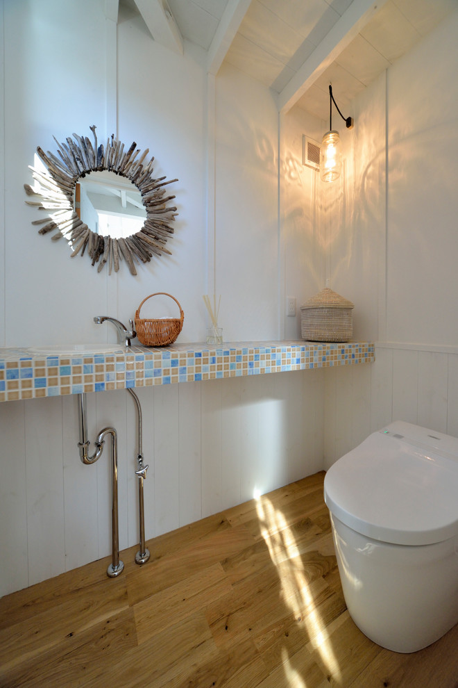 Esempio di un bagno di servizio costiero con pareti bianche, pavimento in legno massello medio, lavabo da incasso e pavimento marrone