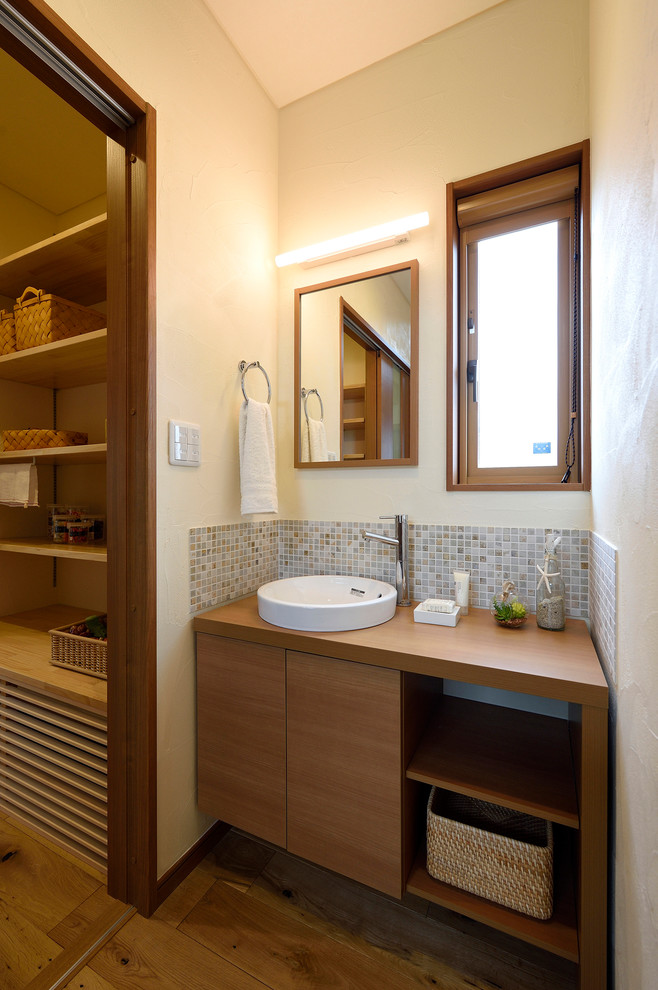 Réalisation d'un WC et toilettes minimaliste en bois brun avec un carrelage multicolore, un carrelage de pierre, un mur blanc, un sol en bois brun, un plan de toilette en bois, une vasque et un sol marron.