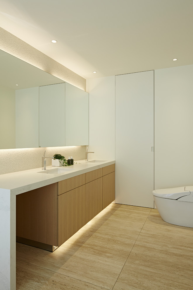 Moderne Gästetoilette mit hellen Holzschränken, Toilette mit Aufsatzspülkasten, beigen Fliesen, weißer Wandfarbe, Travertin, Unterbauwaschbecken, Quarzwerkstein-Waschtisch, beigem Boden, weißer Waschtischplatte und Kassettenfronten in Tokio
