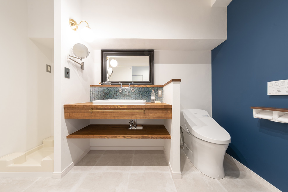 Moderne Gästetoilette mit offenen Schränken, Toilette mit Aufsatzspülkasten, blauen Fliesen, Mosaikfliesen, weißer Wandfarbe, Vinylboden, Unterbauwaschbecken, Waschtisch aus Holz, grauem Boden und brauner Waschtischplatte in Sonstige