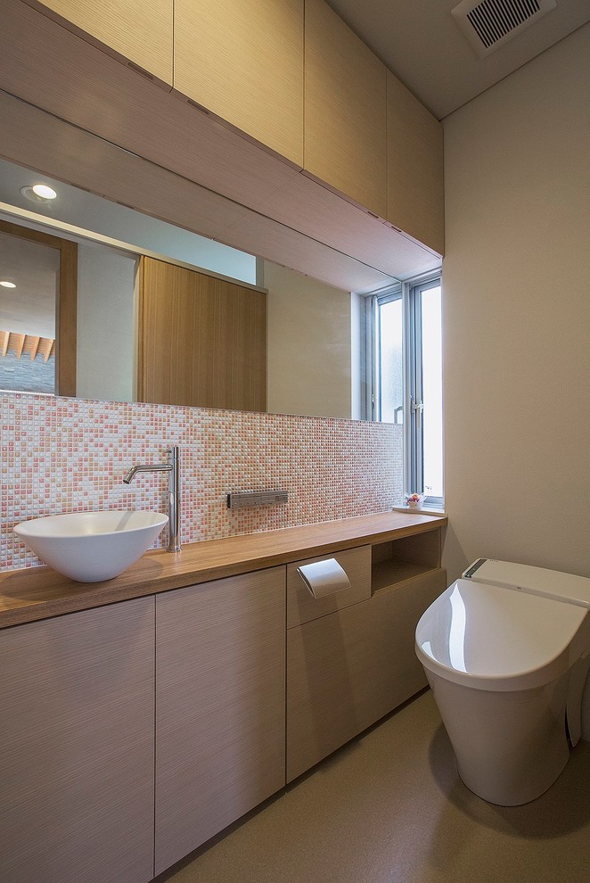 Стильный дизайн: туалет в современном стиле с плоскими фасадами, бежевыми фасадами, оранжевой плиткой, розовой плиткой, белой плиткой, плиткой мозаикой, серыми стенами, настольной раковиной, столешницей из дерева, серым полом и коричневой столешницей - последний тренд
